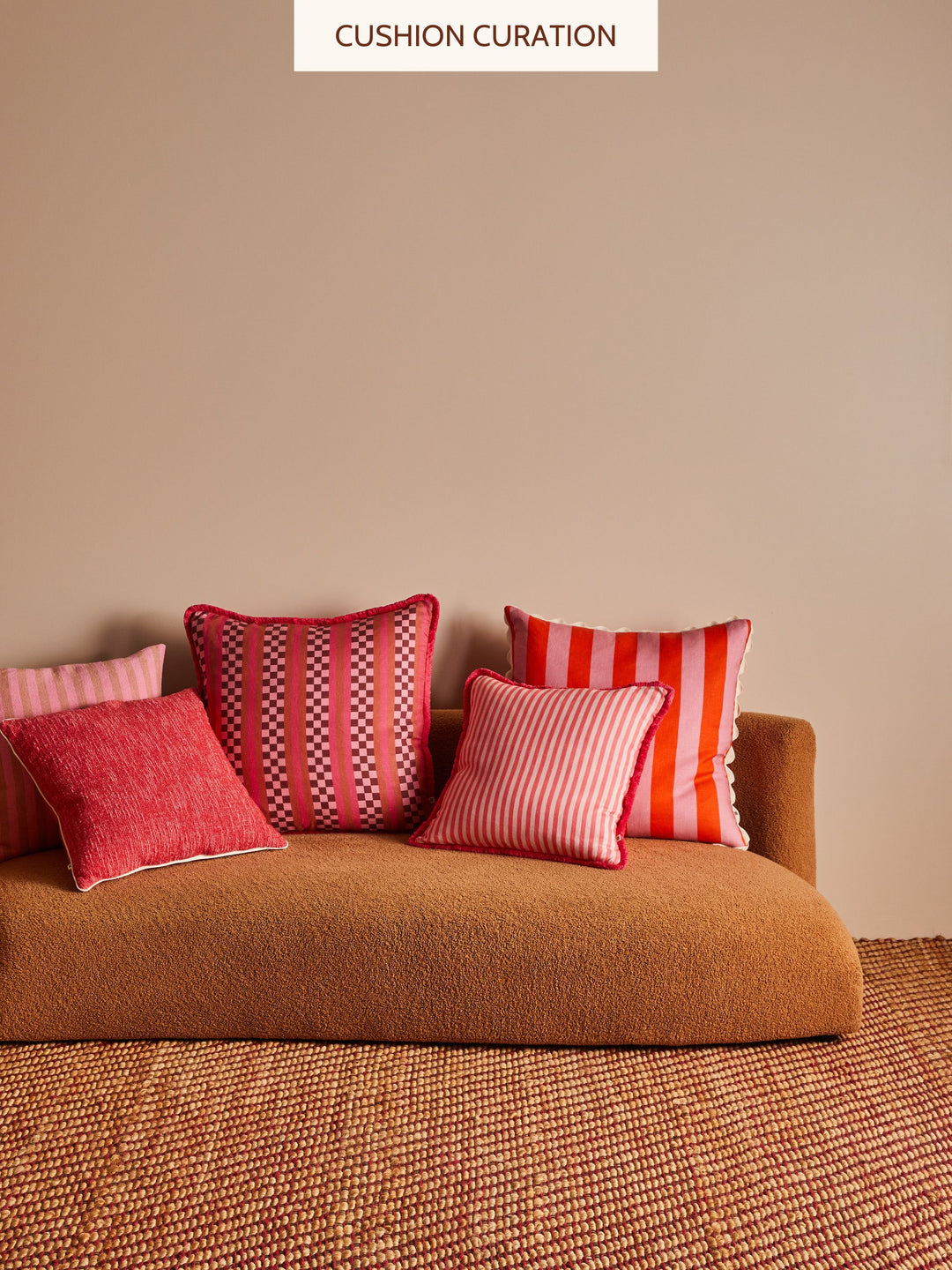 Brown sofa with red and pink patterned cushions against a beige wall.
