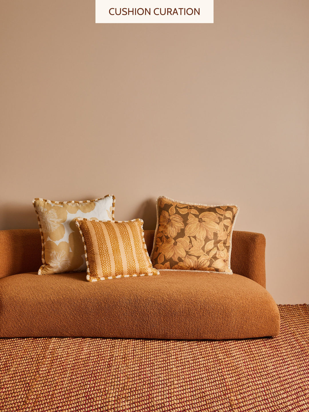 Brown sofa with 3 patterned cushions against a beige wall.