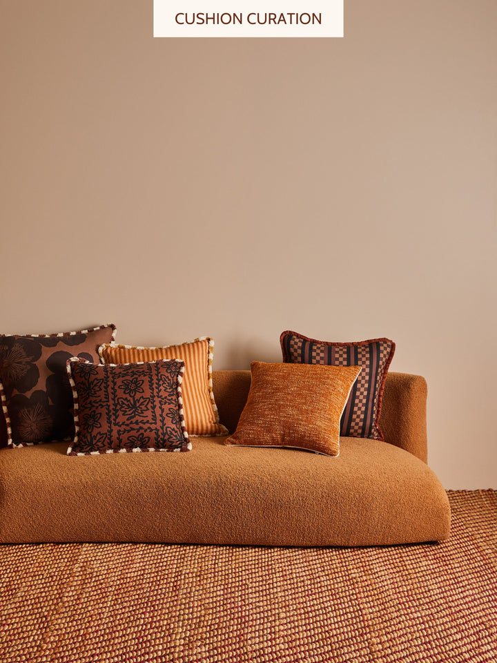 Brown sofa with patterned cushions against a beige wall, labeled 'Cushion Curation'.