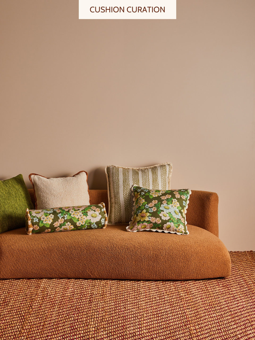 Brown sofa with olive green and natural coloured cushions against a beige wall.