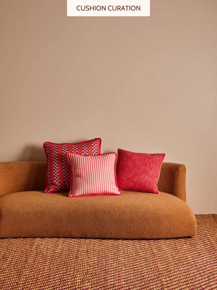 Three pink cushions on a brown sofa against a beige wall 
