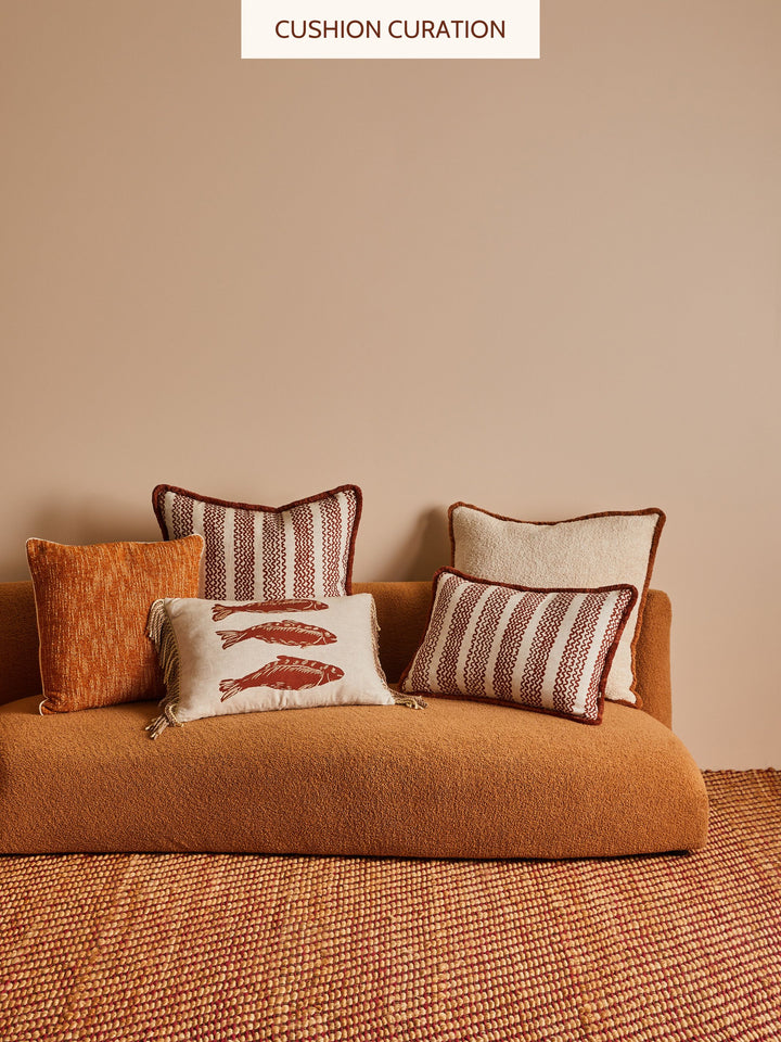 Brown sofa with patterned neutral cushions against a beige wall.
